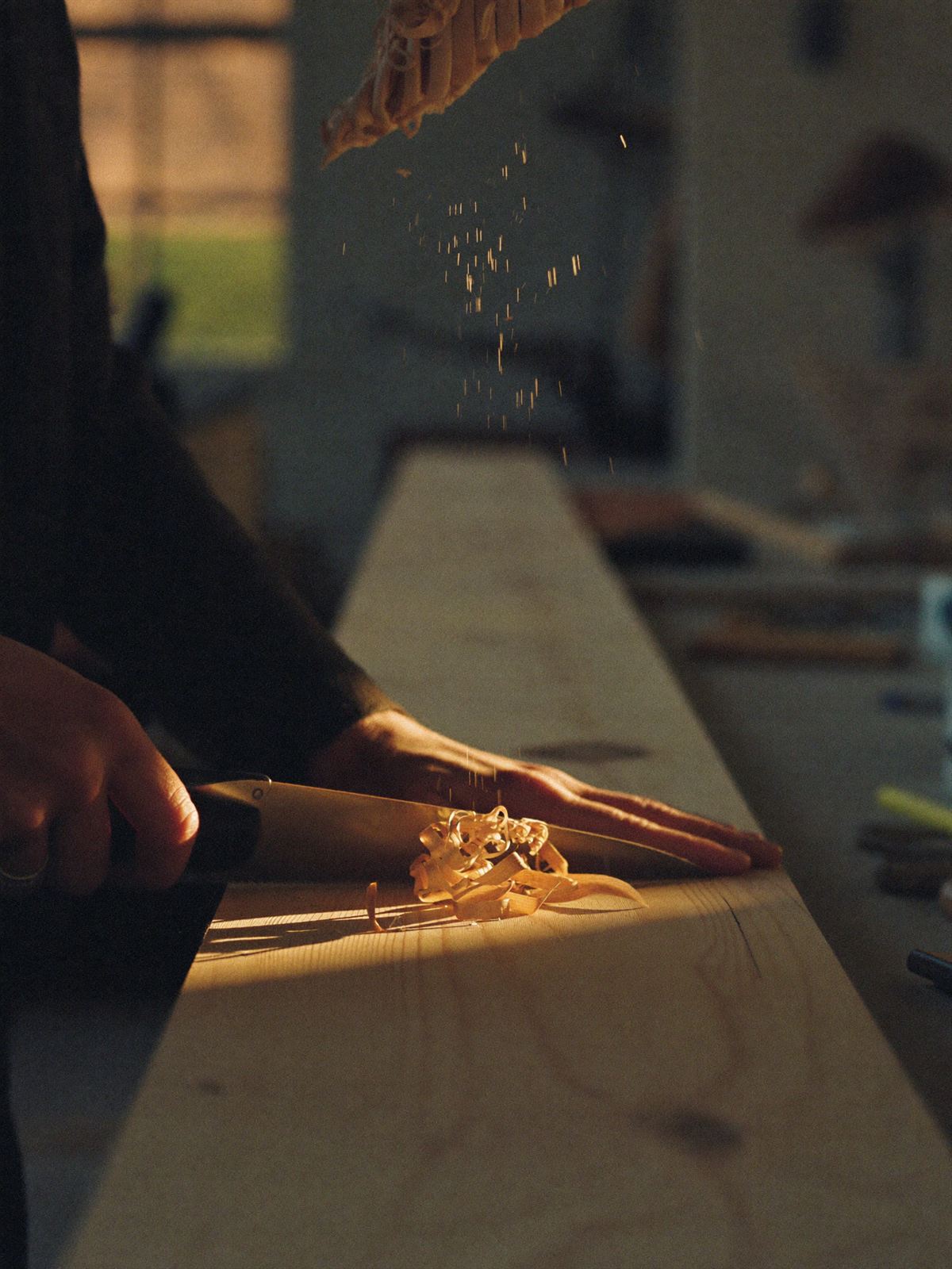 A master joiner planing a length of pale Accoya timber, wood shavings catching the light
